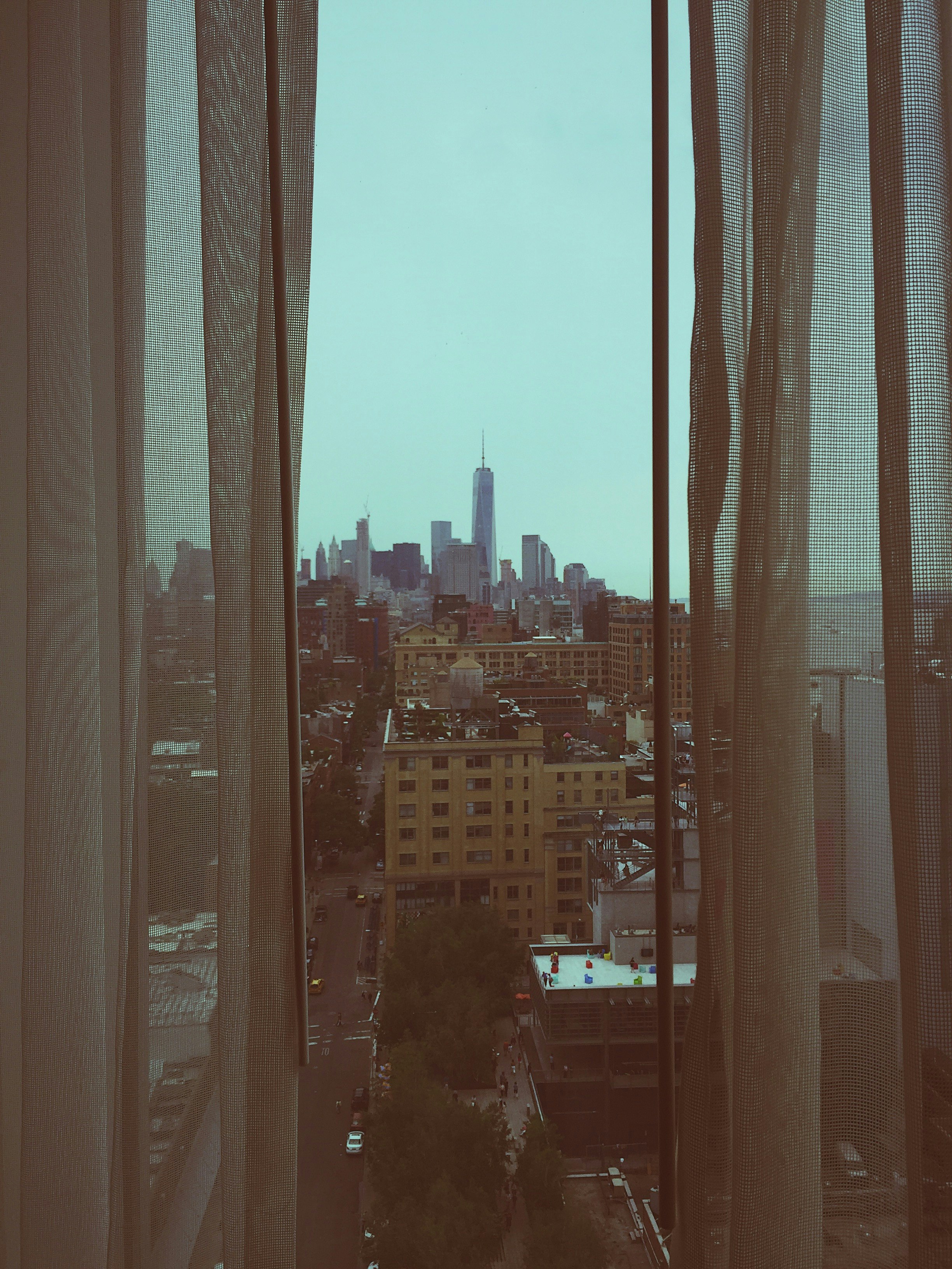 glass window with white curtains overlooking buildings and street with cityscape at distance